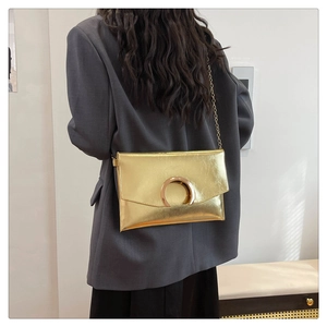 Detail of a shiny gold envelope bag with a large metallic clasp and chain strap