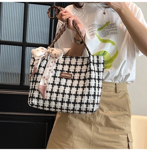 Detail of checkered tote bag with brown leather handles and a decorative pink cherry ribbon
