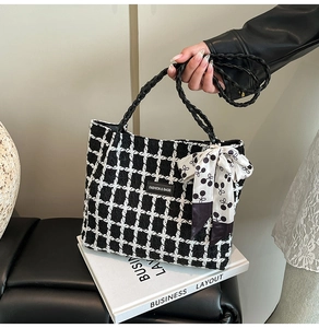 Close-up of checkered wool tote bag with woven handles and a decorative cherry scarf