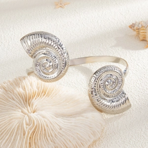 Detailopname van een zilveren nautilus schelp armband op wit zand en koraal