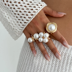 Detail of two gold-finish rings with faux pearls shown on a model's hand
