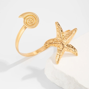 Detailopname van de gouden zeester en schelp manchetarmband op een witte stenen basis