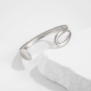 Gedetailleerde opname van een zilveren gebogen armband op een witte getextureerde steen