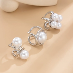 Macro shot of silver metal ear cuffs with white faux pearls on a minimalist background