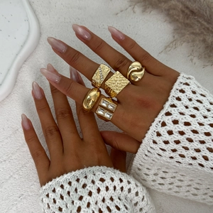 Détail d'un ensemble de bagues dorées empilables avec strass sur fond de tissu blanc épuré