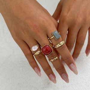 Macro detail of 5-piece gold ring set featuring red square gem and textured bands on hand