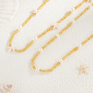 Détail d'une chaîne de taille océan avec perles dorées, étoiles de mer blanches et perles