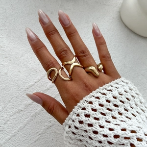 Detail eines vierteiligen unregelmäßigen Goldring-Sets an der Hand mit Strickhintergrund