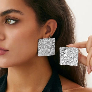 Detailed view of silver square earrings with unique hammered foil texture on female model