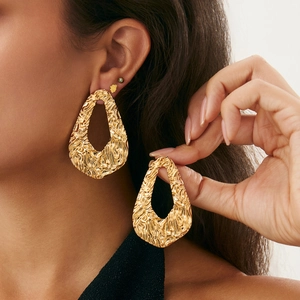 Macro detail of large gold-toned hollow drop earrings with wavy metallic texture