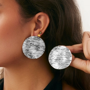 Close-up of oversized silver textured round earrings showing ripple pattern on ear
