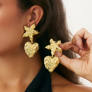 Detailed view of gold starfish and irregular hammered heart drop earrings on model