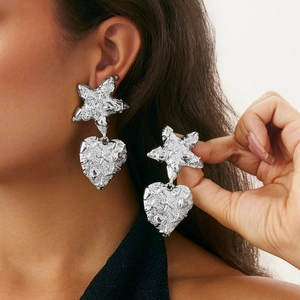 Close-up of model wearing oversized silver heart earrings with textured star accents