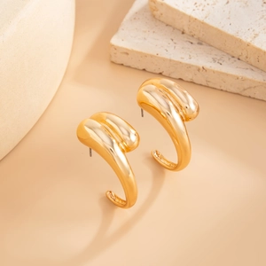 Detail view of gold irregular C-shape earrings on natural stone decorative background