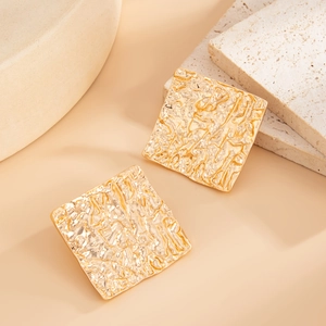 Close-up of golden square earrings with unique liquid lava texture and hammered finish