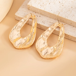 Close-up of oversized gold textured drop earrings on natural travertine stone