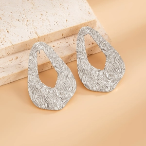 Macro shot of silver U-shaped earrings with irregular hollow design on beige stone