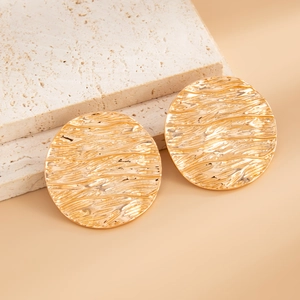 Macro detail of U-shaped gold earrings with irregular pleated texture on marble