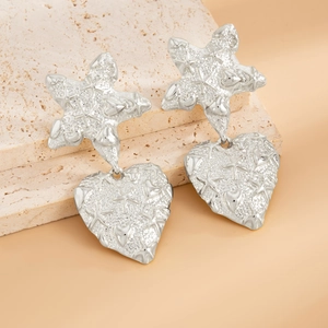 Detailed close-up of silver earrings with starfish and heart motifs on textured metal