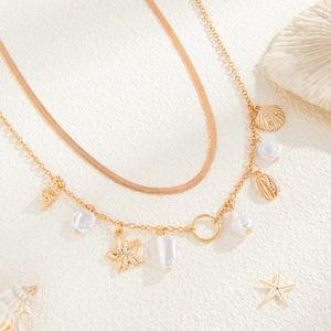 Detail of layered gold waist chain with pearls, starfish, and seashell charms on sand