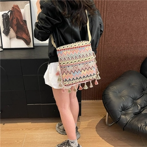 Détail d'un sac bandoulière tissé bohème avec des pompons colorés et motifs géométriques