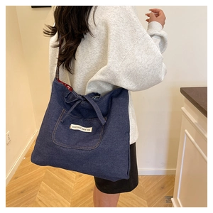 Detail of blue denim tote bag with functional front pocket and decorative bow drawstring