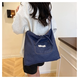 Detail of blue denim tote bag with functional front pocket and decorative white textile label