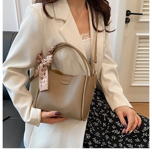 Close-up of khaki pebbled leather bucket bag featuring a decorative plaid silk scarf handle
