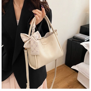 Detail of lychee pattern leather bucket bag with woven handle and bow ribbon accessory