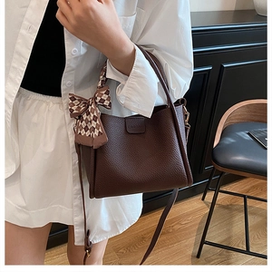 Detail of dark brown litchi grain handbag with a checkered silk scarf and logo