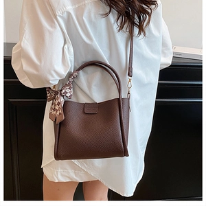 Detail of dark brown pebble leather tote bag with elegant plaid silk scarf on the handle