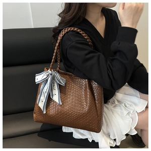 Close-up of brown woven leather tote with decorative silk scarf and braided handle
