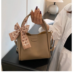 Close-up of khaki litchi grain bucket bag with decorative plaid ribbon and fashion logo
