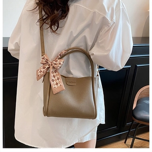 Detail view of a taupe leather bucket bag featuring a decorative plaid silk scarf handle