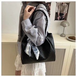 Detail of black woven tote bag featuring a decorative printed silk scarf on the handle
