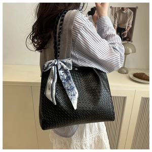 Detail of black woven tote bag featuring a decorative floral silk scarf on the handle