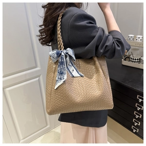 Detail of khaki woven tote bag with silk scarf accessory on a shoulder strap