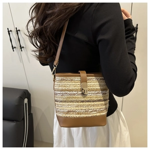 Detailed side view of a woven straw bucket bag with brown leather strap and gold buckle