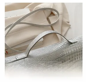 Detailed macro view of silver crocodile embossed texture on a sleek underarm handbag