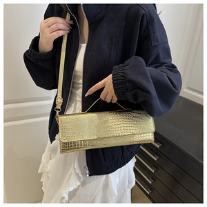 Detail of gold crocodile texture handbag with chain strap shown on navy blue outfit