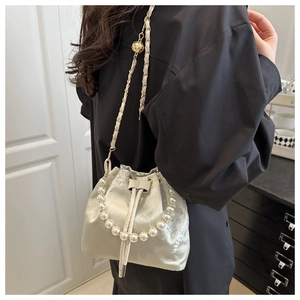 Detail of champagne satin bucket bag with floral embroidery and pearl handle worn crossbody