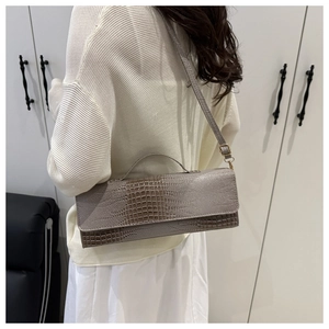 Detail view of taupe crocodile embossed shoulder bag worn by model in minimalist setting