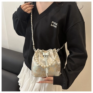 Detailed shot of bucket bag with gold Chinese embroidery and elegant pearl handle