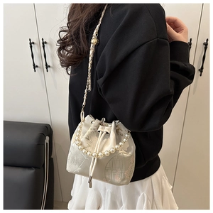 Detail of embroidered bucket bag with pearl handle and bamboo pattern on ivory fabric