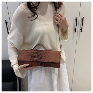 Detail view of brown crocodile texture handbag showing glossy finish and sleek shoulder strap
