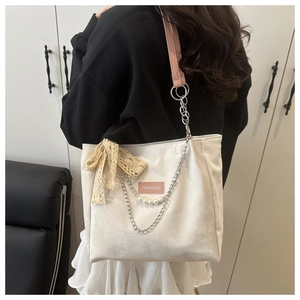 Detail of cream tote bag featuring pink straps with lace bow and pearl chain accessories