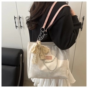 Detailed view of beige tote bag with pink straps, pearl chain, and lace bow accent