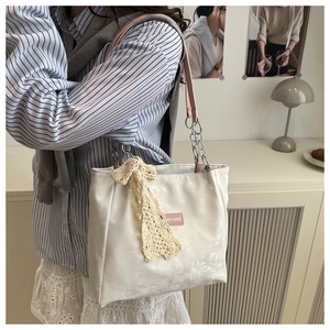 Detail of velvet tote bag featuring a lace bow and chain shoulder strap on a model