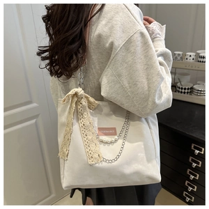 Detail of white tote bag featuring lace bow, pearl chain and pink shoulder strap