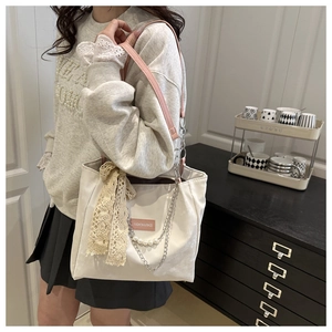 Detail of white tote bag featuring pink straps, pearl chain, and lace scarf accent